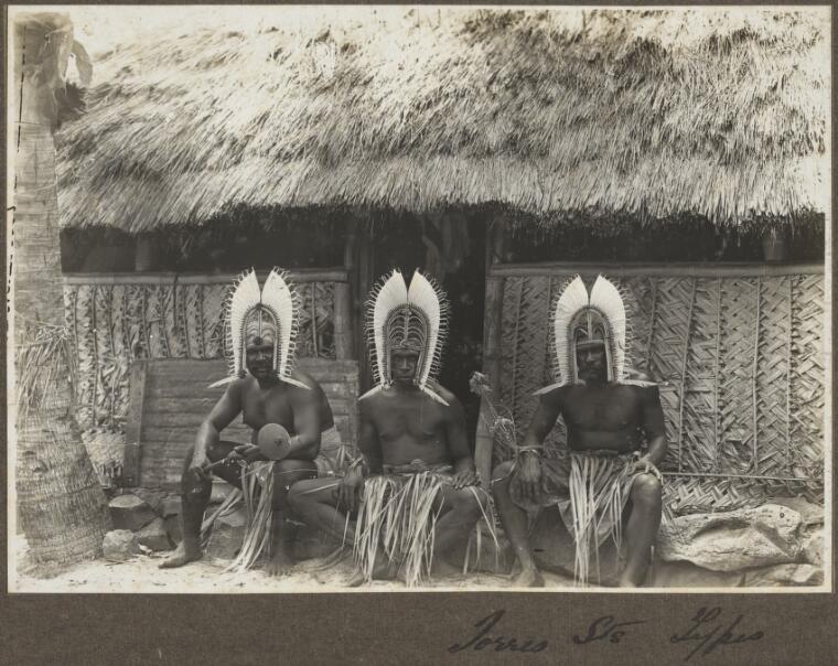 Torres Straits types [three men wearing head dresses sitting outside hut] [picture] 1921