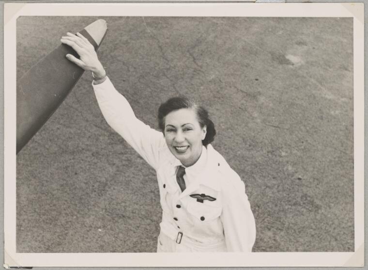  Australian Women Pilots' Association member Nancy Leebold (nee Ellis) in flying suit holding onto an aeroplane's propeller, May 1954 [picture].