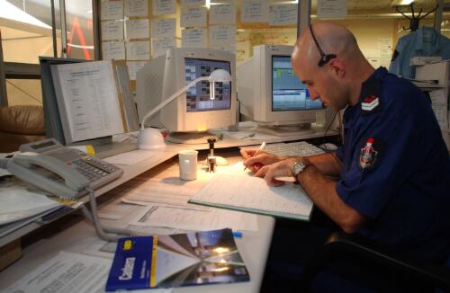 An officer from Emergency Services Agency, writing on a notebook at his desk, Curtin, Canberra, January 2003 [picture] / Damian McDonald