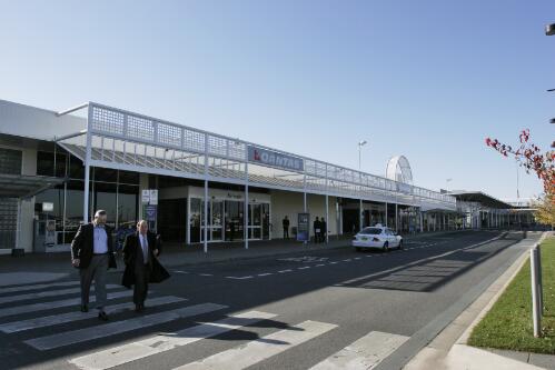 Exterior view of Canberra Airport terminal with unidentified individuals crossing the road, 8 June 2005 [picture] / Loui Seselja