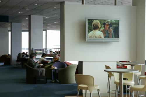 A large screen television and passengers in the background, inside Virgin Blue's lounge "The Blue Room", Tullamarine Airport, Melbourne, 21 June 2005 [picture] / Damian McDonald