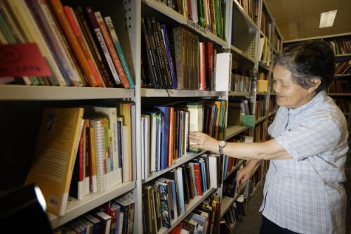 Xingsu Shen, volunteer in the Chinese Unit, working in the Asian Collections stacks examining collection material, 2006 [picture] / Greg Power