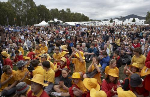 Crowds sitting on the grass outside Parliament House, with school children wearing red and yellow uniforms in the foreground, at the Apology to the Stolen Generations of Australia, Canberra, 13 February 2008 [picture] / Greg Power