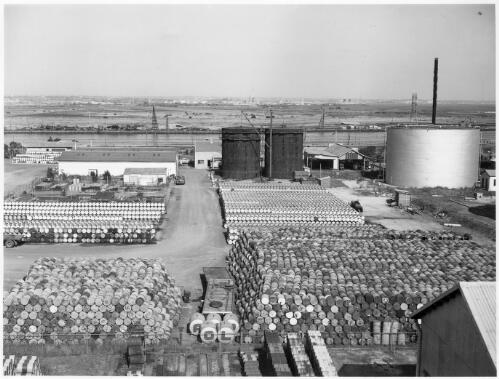 A view of the north yard looking due east showing Tank 23, with stocks of empty white product containers in foreground and stocks of lubricating oil drums, the stores building and two 800 ton  bulk lube oil tanks and other oil tanks under construction, Newport Depot, Victoria, January 1954 [picture] / Gordon F. De Lisle
