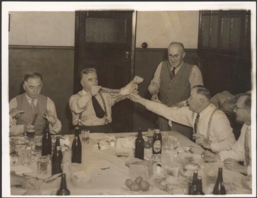 [Sir Robert Menzies at dinner holding a cooked crab by its claws, in Launceston Tasmania, with "Examiner" colleagues.] [picture]