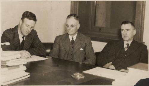 [John Curtin, M.H.R. (centre) seated at a desk between Mr Thompson, MP (left), and Mr Richardson, Leader of the Opposition (right) at Gawler Town Hall on 21 November 1938] [picture]