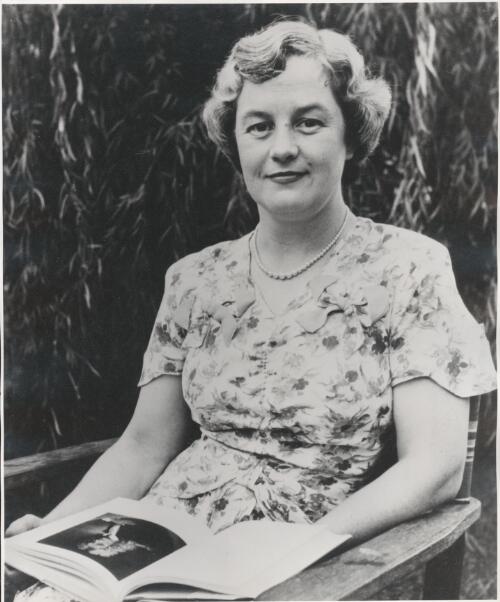 Portrait of Mavis Thorpe Clark, sitting with open book on lap [picture] / photography by Athol Shmith