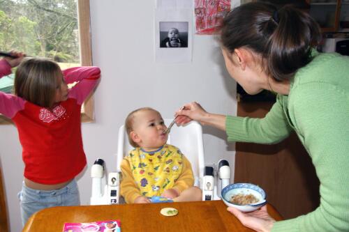Nat at home feeding her toddler, Jet, as cousin Pia looks on while brushing her hair, Dandenong Ranges, Victoria, 2006 [picture] / Lee Grant