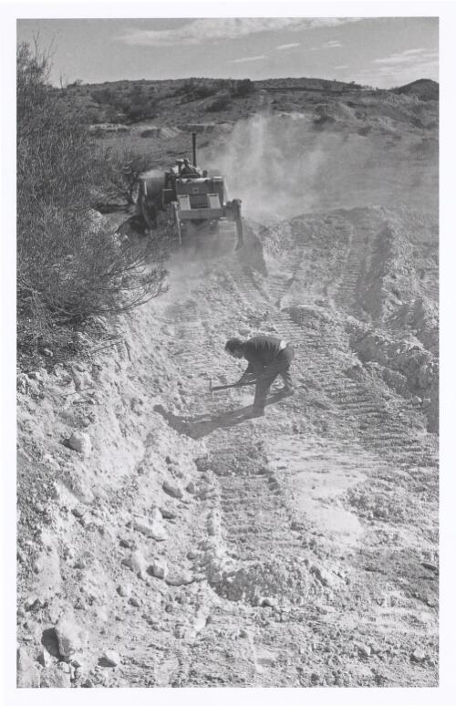 An excavator levels the ground while a man picks the newly dug surface, Coober Pedy, South Australia, 1970 [picture] / Jeff Carter
