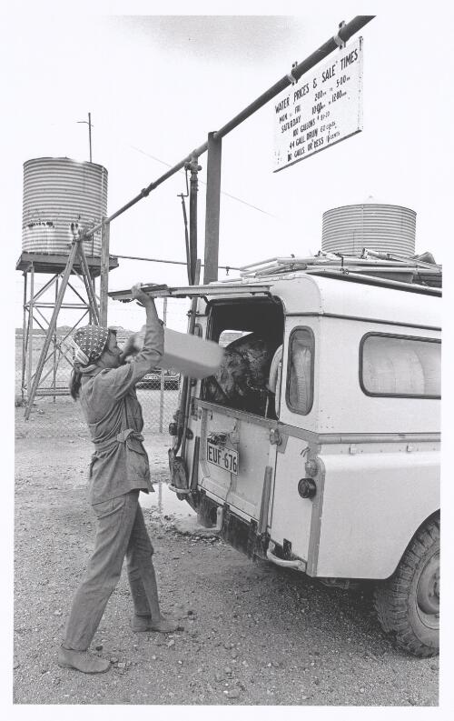 A woman loads a jerry can of water into her Land Rover at Coober Pedy, South Australia, 1970 [picture] / Jeff Carter