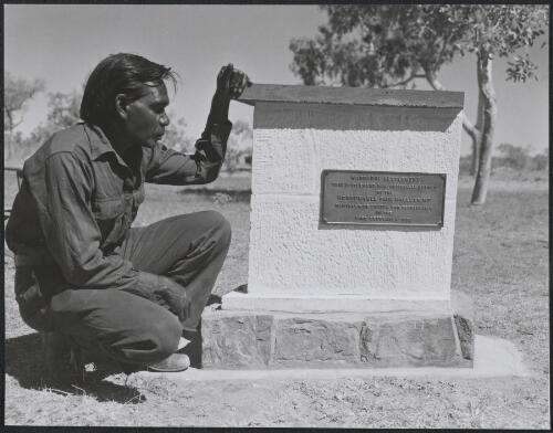 An Aboriginal man crouches beside a plaque commemorating the official opening of the Warrabri Settlement, Northern Territory, ca. 1958 [picture]
