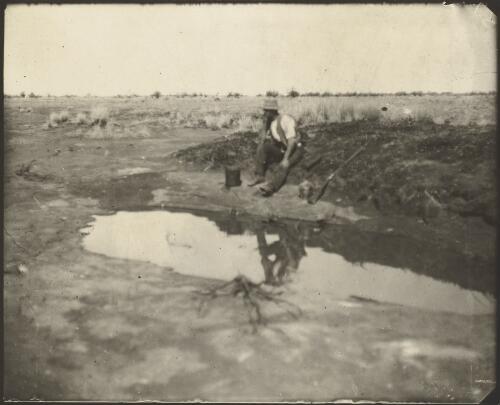 Man seated beside a flat rock water hole which saved the lives of Captain S.A. White's party when entering into the Everard Ranges, Central Australia, 1913 [picture] / Captain S.A. White