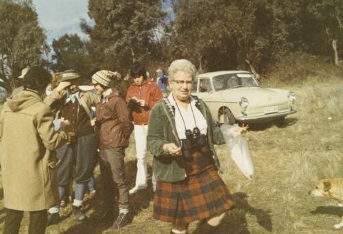 Nancy Burbidge, on field location with binoculars, ca. 1970 [picture]