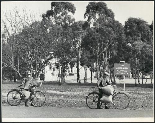 A woman and a man carrying sacks on their bicycles in front of the H.C. Coombs Building at the Australian National University, Canberra, ca. 1965 [picture] / Ted Richards