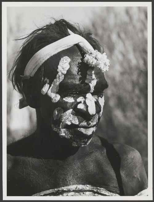 Jimmy Jibarula of the Wailbri language group with his face painted in white ochre and wearing a kukulpas or marrapintis, his headdress, preparing for the Murrungurru dance, Yuendumu, Northern Territory, 24 January 1973 [picture] / Michael Jensen