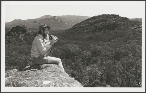 Archaeologist Ben Gunn sitting on a ledge searching for sandstone outcrops, Grampians, Victoria, 19 January 1984 [picture] / John McKinnon