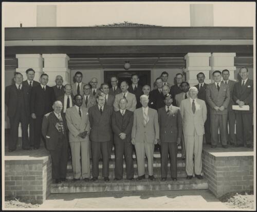 Group of delegates including Sir Stanley Carver at an economic forum, standing on the steps of the Hotel Canberra, Australian Capital Territory, circa 1950 / Australian News & Information Bureau Photograph