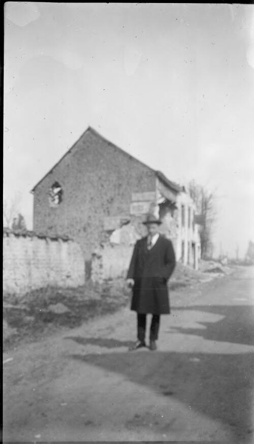 P.E. Deane in a hat and overcoat walking down a village street, post WWI France [?] [picture]
