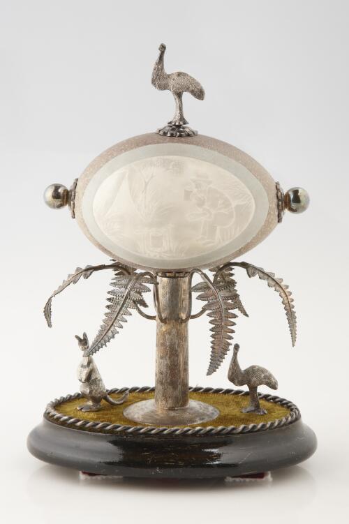 [Carved emu egg on silver-plate and wood stand with fern, kangaroo and emu decoration] [realia]