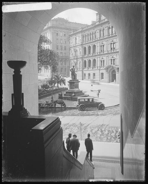 Inside entrance of Kyle House looking across Macquarie Place and statue of Governor Macquarie to Lands Department in Bridge Street, Sydney [picture] / Harold Cazneaux