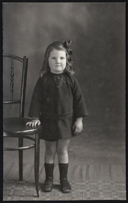 Portrait of unidentified young girl wearing dark dress with floral embroidery, standing next to chair, Tumut, New South Wales [picture] / R.C. Strangman