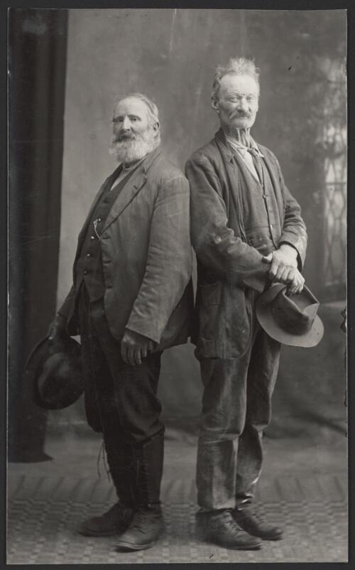 Portrait of two elderly men wearing suits posed back to back looking to the camera, Tumut, New South Wales [picture] / R.C. Strangman