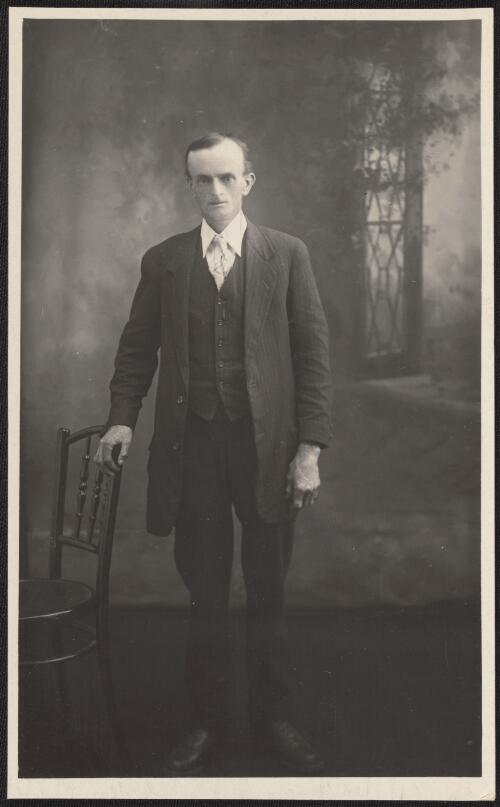 Portrait of a man in a long jacket, hand on chair, Tumut, New South Wales  / R.C. Strangman