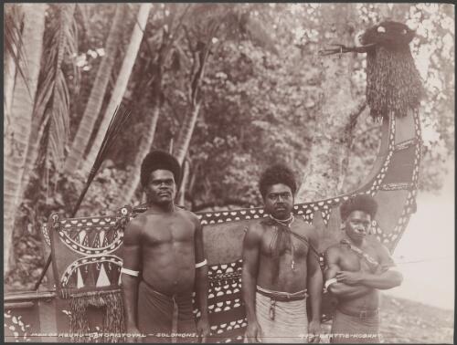 Three men standing in front of a painted canoe at Heuru, Solomon Islands, 1906 / J.W. Beattie