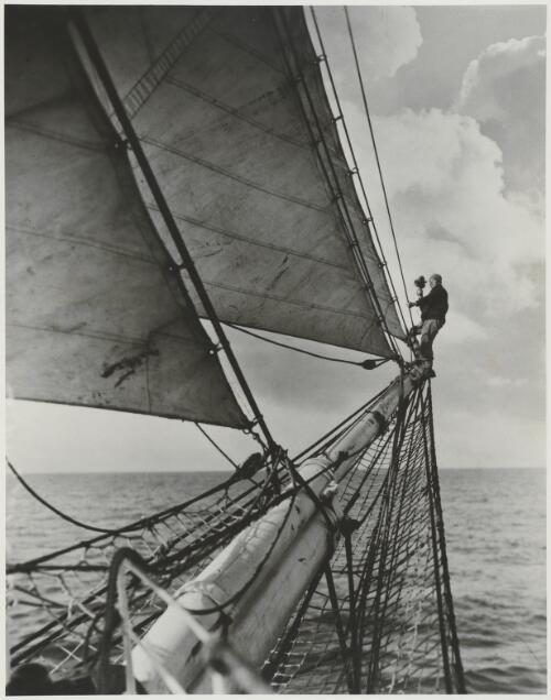 Frank Hurley, official photographer to the B.A.N.Z. Antarctic Research Expedition, filming from the tip of the Discovery's jib-boom, ca. 1930 [picture]