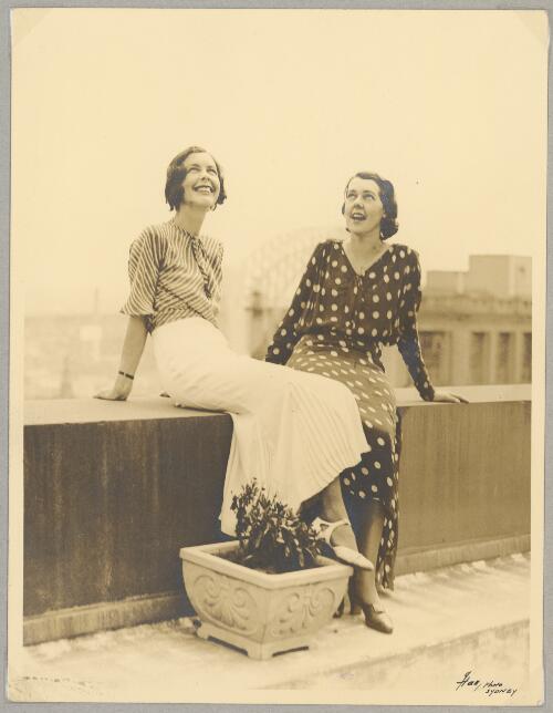Portrait of two unidentified women sitting on a rooftop ledge with the Sydney Harbour Bridge in background, ca. 1940s [picture]