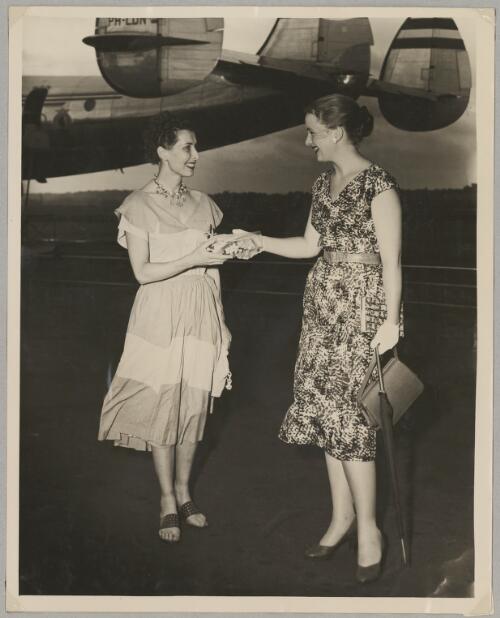Annette Anderson handing a gift to Dutch pilot Liane Latour standing in front of the tail of Lockheed L-749A Constellation airliner PH-LDN on an airport tarmac, Sydney, 18 January 1955 [picture]