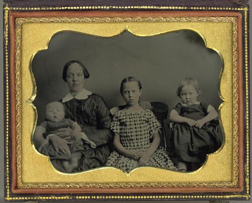 Unidentified woman with a baby in her lap and two children, all seated in a studio [picture]