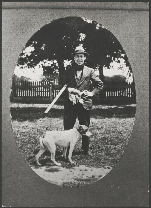 Man holding a shotgun and birds with a hunting dog at his feet, ca. 1925, [picture]