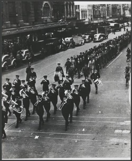 Uniformed brass band marches in front of men parading down a city street in Melbourne, ca. 1940 [picture]
