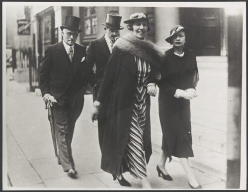 Two couples dressed for an occasion walking along a street, ca. 1930 [picture]