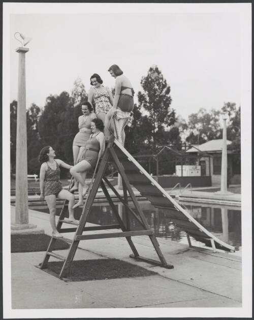 Models in swimsuits pose on a water slide at a swimming pool, ca. 1940 [picture]