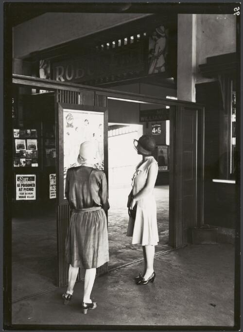 Two women at a railway station looking at a poster advertising clothing, Melbourne, ca. 1923 [picture]