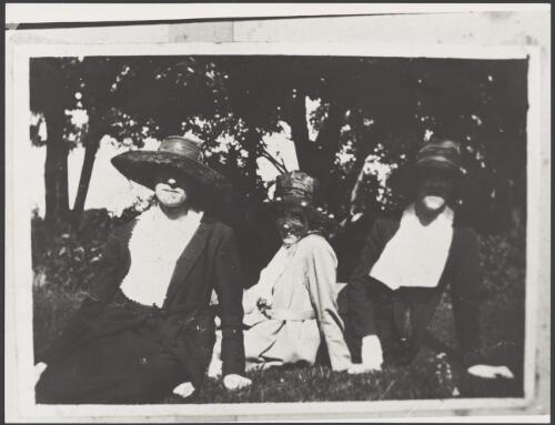 Three women wearing wide brimmed hats sitting on the lawn in a garden, ca. 1925 [picture]
