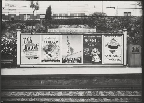 Advertising billboard for Old Court whisky, Cadbury's chocolate, Dickie's towels, Pick-me-up Worcestershire sauce and Akubra hats on railway platform, Melbourne, ca. 1930 [picture]