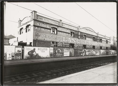 Advertising billboards for Lane's Emulsion, P&O services to Durban, Cape Town and London, Rolfes tea, Kingston and Lord, sellers of umbrellas and walking sticks, Renardi pianos, the Tivoli Theatre, Oshkosh overalls, Abbots lager and Preservene soap on railway platform and wall, East Richmond, Victoria, ca. 1930 [picture]