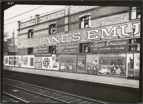 Advertising billboards for Lane's Emulsion, Robur tea, Uncle Toby's oats, Oshkosh overalls and Harding's Healesville Sauce on railway platform and wall, East Richmond, Victoria, ca. 1930 [picture]