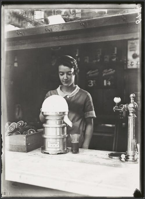 Woman using a Sunkist juicing machine at a fruit stall, on a railway station, Melbourne, ca. 1925 [picture]