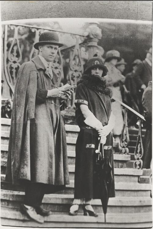 Man in a collared cape and a woman in a short sleeved dress and fur stole in the stands at the Melbourne Cup, Melbourne, 1921 [picture]
