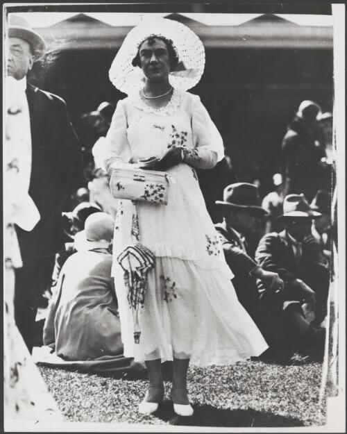 Woman wears an embroidered white dress and carries a matching bag and umbrella at the Melbourne Cup, Melbourne, 1931 [picture]