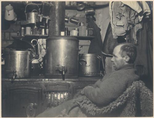 [Man sitting by a kitchen stove, Australasian Antarctic Expedition, 1911-1914] [picture] / Wild