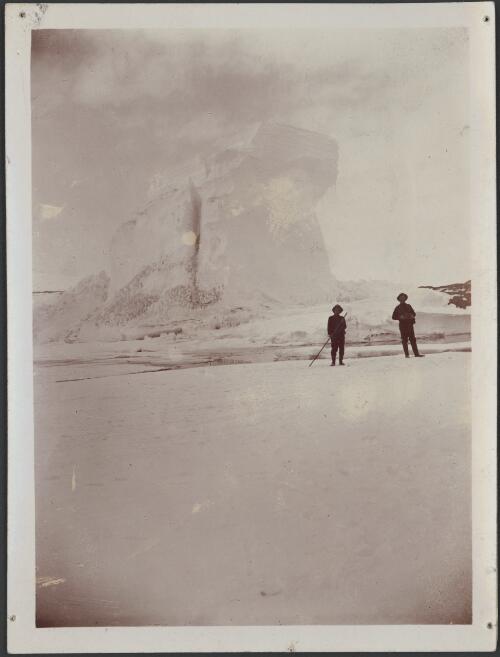 [Two men standing in front of a large iceberg, Australasian Antarctic Expedition, 1911-1914] [picture]