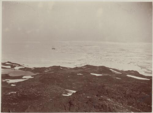 [Looking out from rocky foreground at a boat caught in pack ice, Australasian Antarctic Expedition, 1911-1914] [picture]