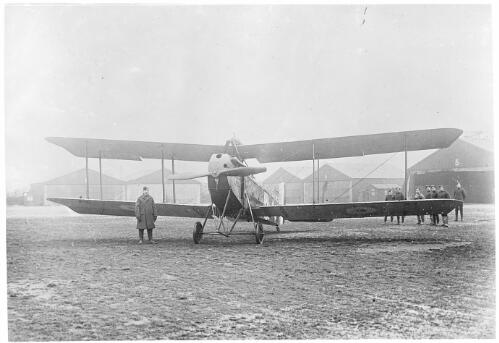 One man standing in front of and a group of men standing beside a single engined bi-plane, serial number B 5782 with British markings, France, ca. 1916 [picture]