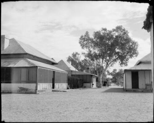 Three people standing beside a tree near three buildings, Northern Territory, 1947 [picture] / E.W. Searle