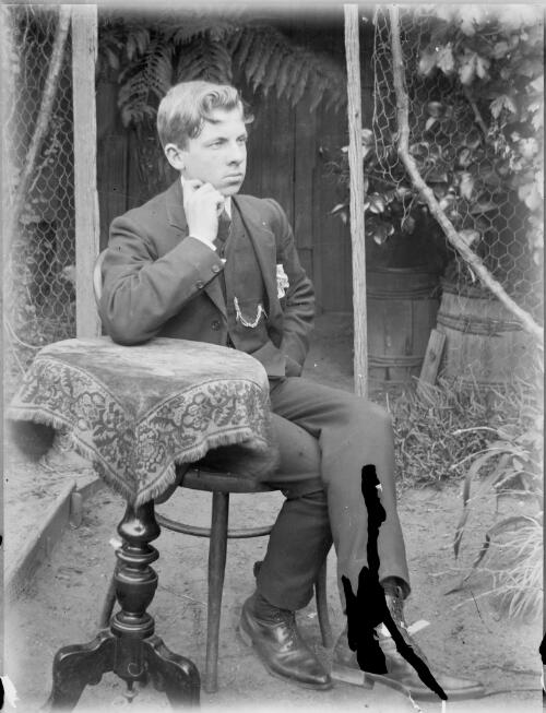 Young man seated at a table in a garden, Australia, ca. 1900 [picture]